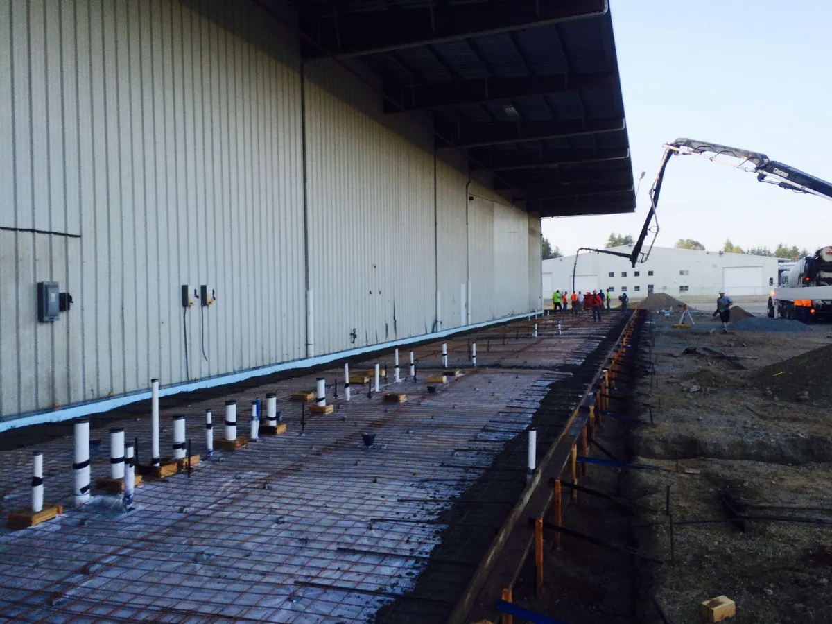 Concrete slab and utility preparation beside a commercial steel building in Western Washington