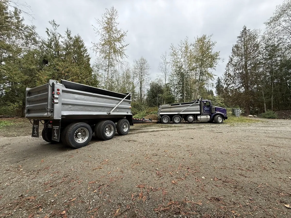 Dump trucks staged on a gravel site for material hauling and access planning in Western Washington