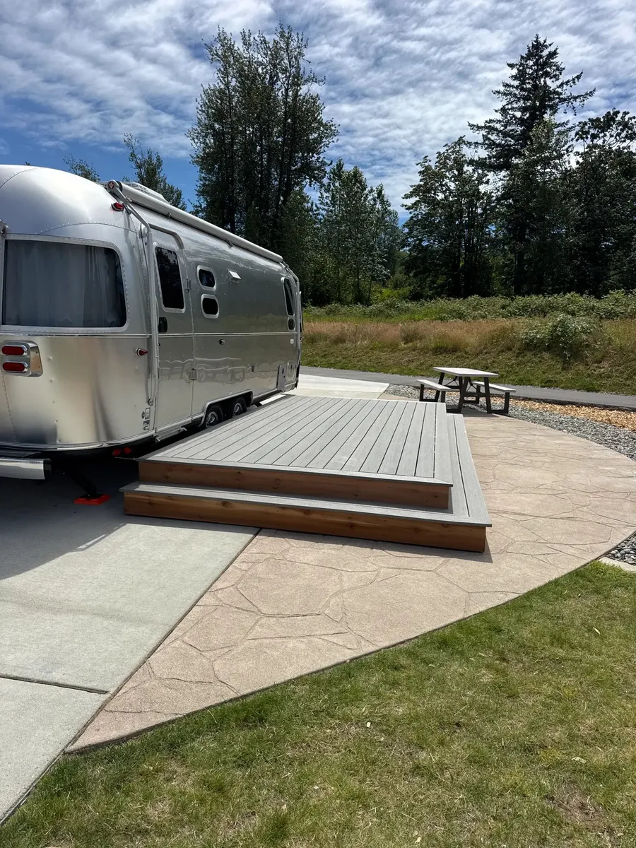 Completed TimberTech composite deck with cedar skirting and stepped access beside an Airstream rental unit at Angel of the Winds RV Resort, with trees and picnic table in background
