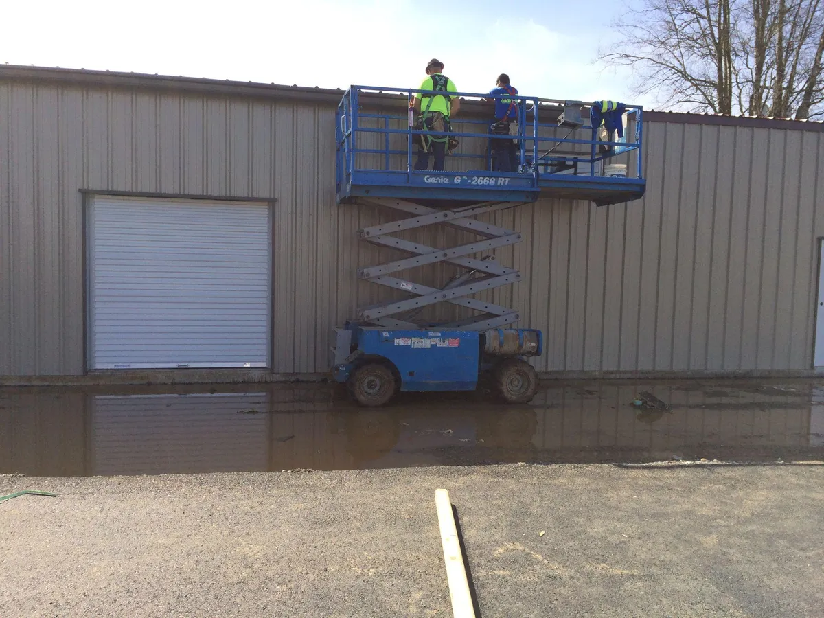 Workers in safety vests on a scissor lift performing exterior work on a steel building