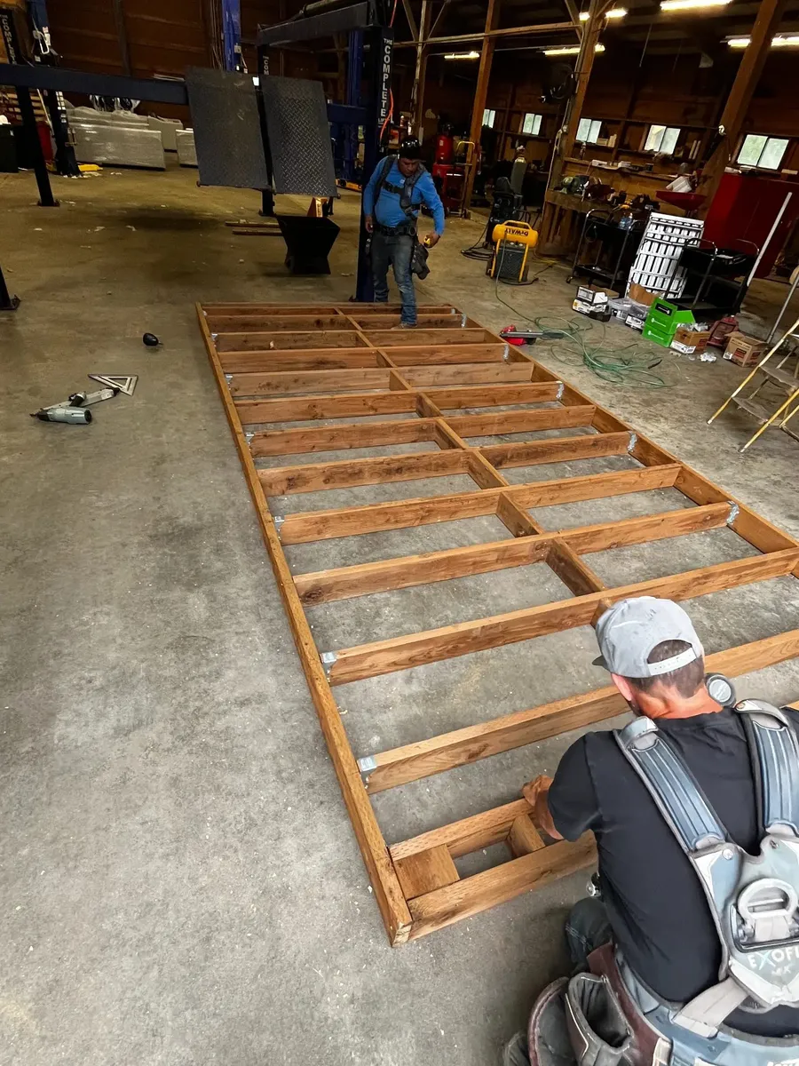 Two Pilchuck Construction crew members assembling a cedar deck frame with metal brackets inside the company shop in Arlington, Washington