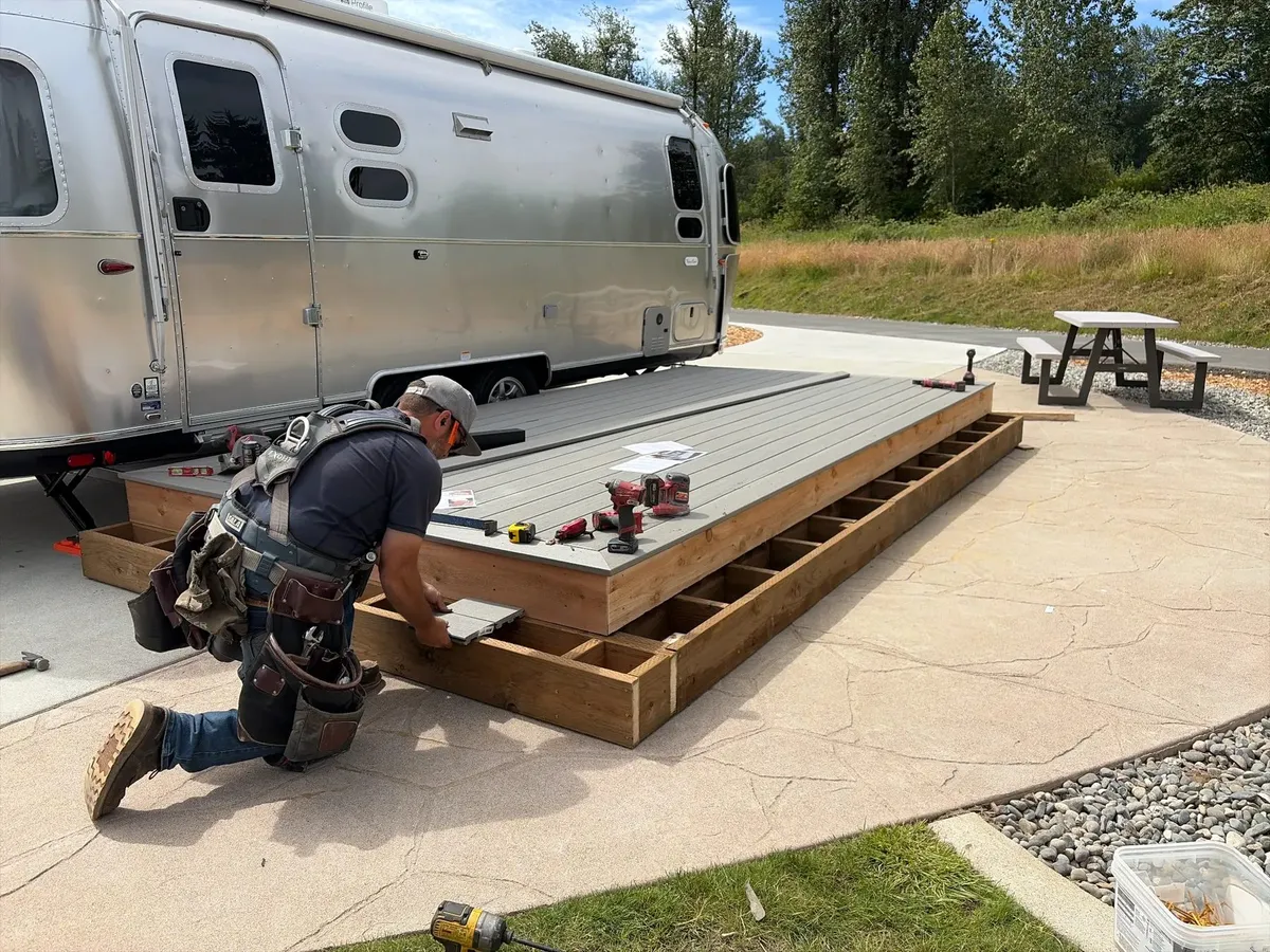 Pilchuck Construction crew member installing TimberTech composite decking on a low-profile deck frame beside an Airstream trailer at Angel of the Winds RV Resort in Arlington, Washington