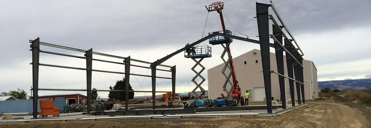 Crew erecting a pre-engineered steel building frame using scissor lifts and a telehandler