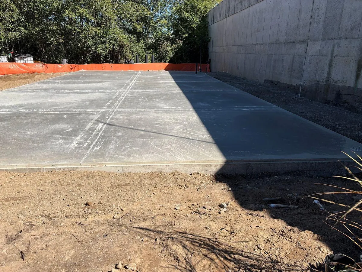 Concrete foundation slab at the Summer Gardens shop site in Edmonds, Washington, viewed across bare ground.