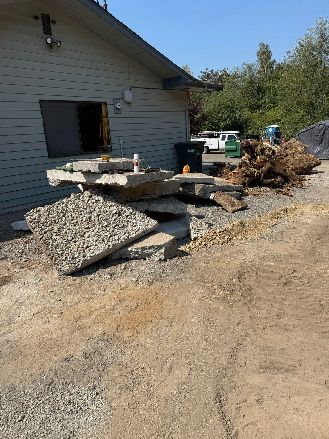 An uprooted stump and broken concrete slabs on cleared ground at the Somerset Gardens project site in Edmonds, Washington.