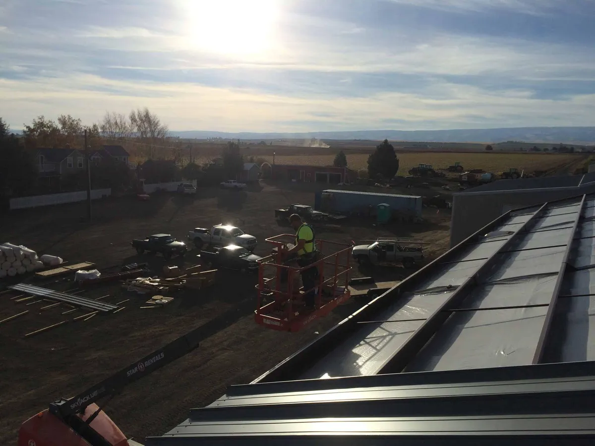 Worker on a scissor lift near a steel building roof with a broad construction site view in Western Washington